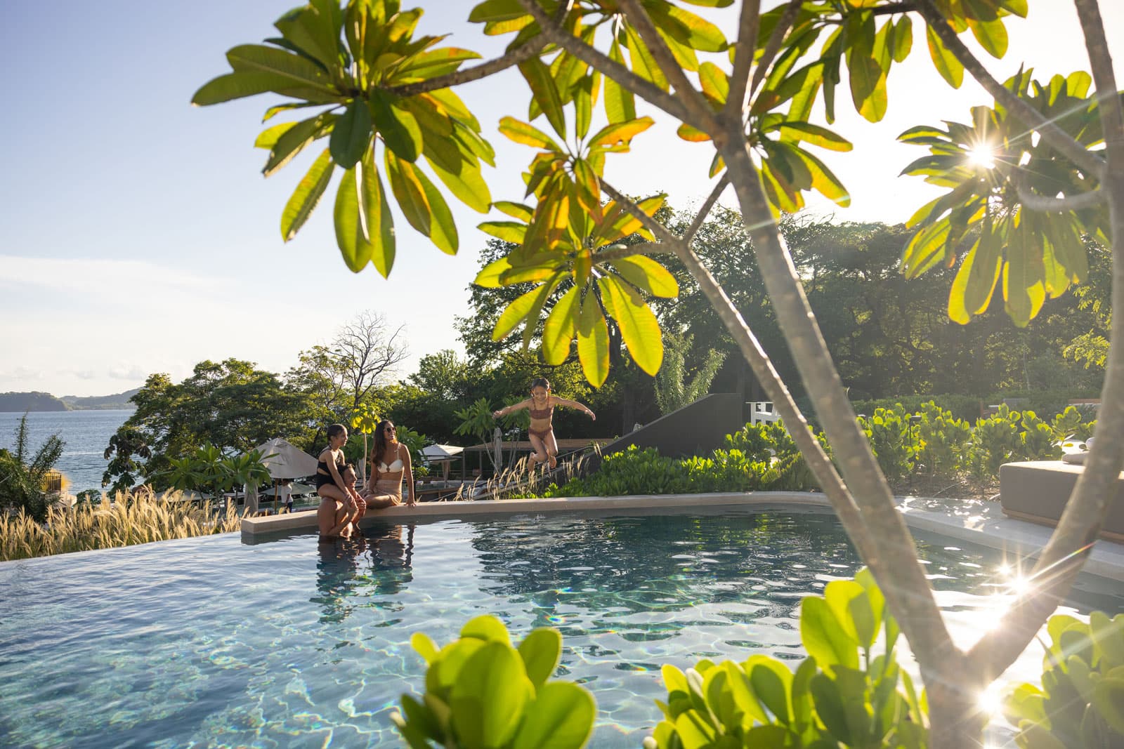 Waldorf Astoria Punta Cacique Costa Rica multi-level pool area. A family of four is in the pool. They are surrounded by lush tropical landscaping with the ocean in the background.