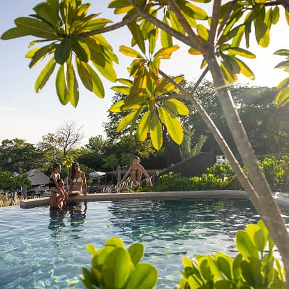 Waldorf Astoria Punta Cacique Costa Rica multi-level pool area. A family of four is in the pool. They are surrounded by lush tropical landscaping with the ocean in the background.