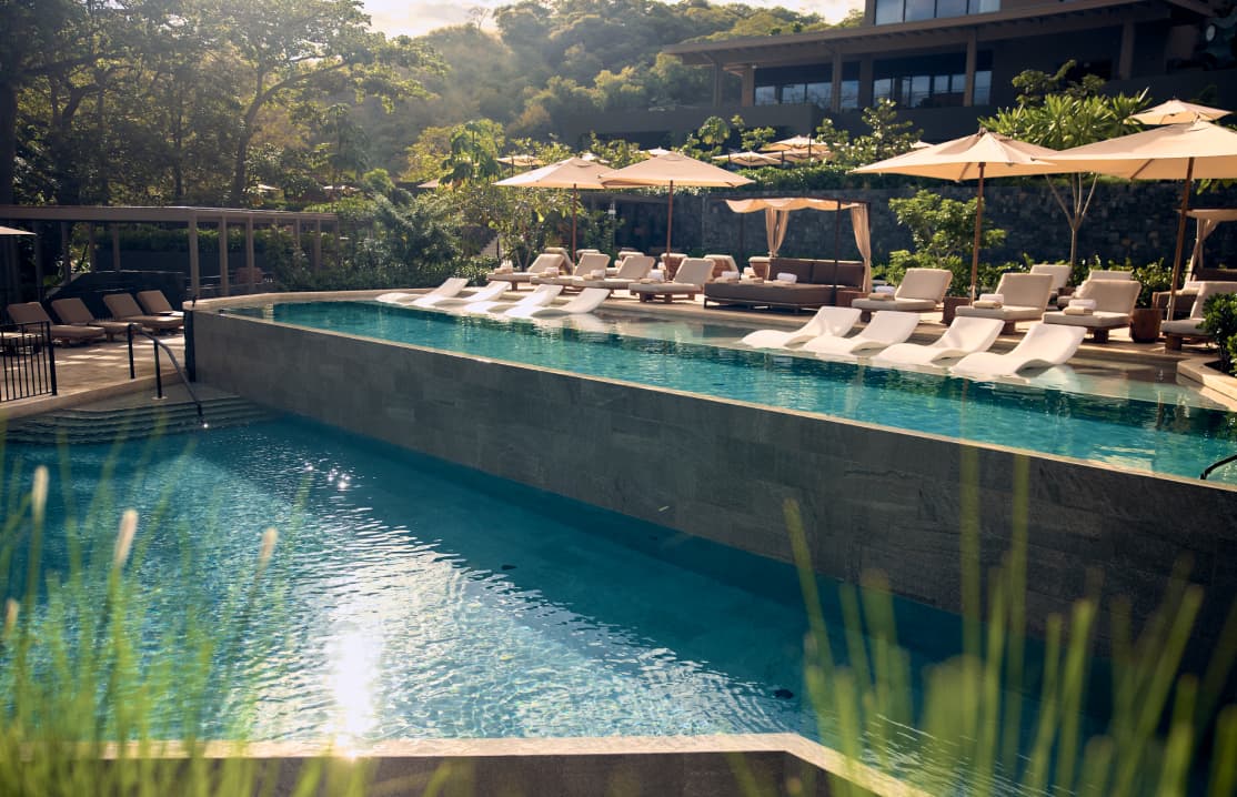 Multi-level infinity pools cascading down a hillside, surrounded by palm trees and overlooking the Ocean.