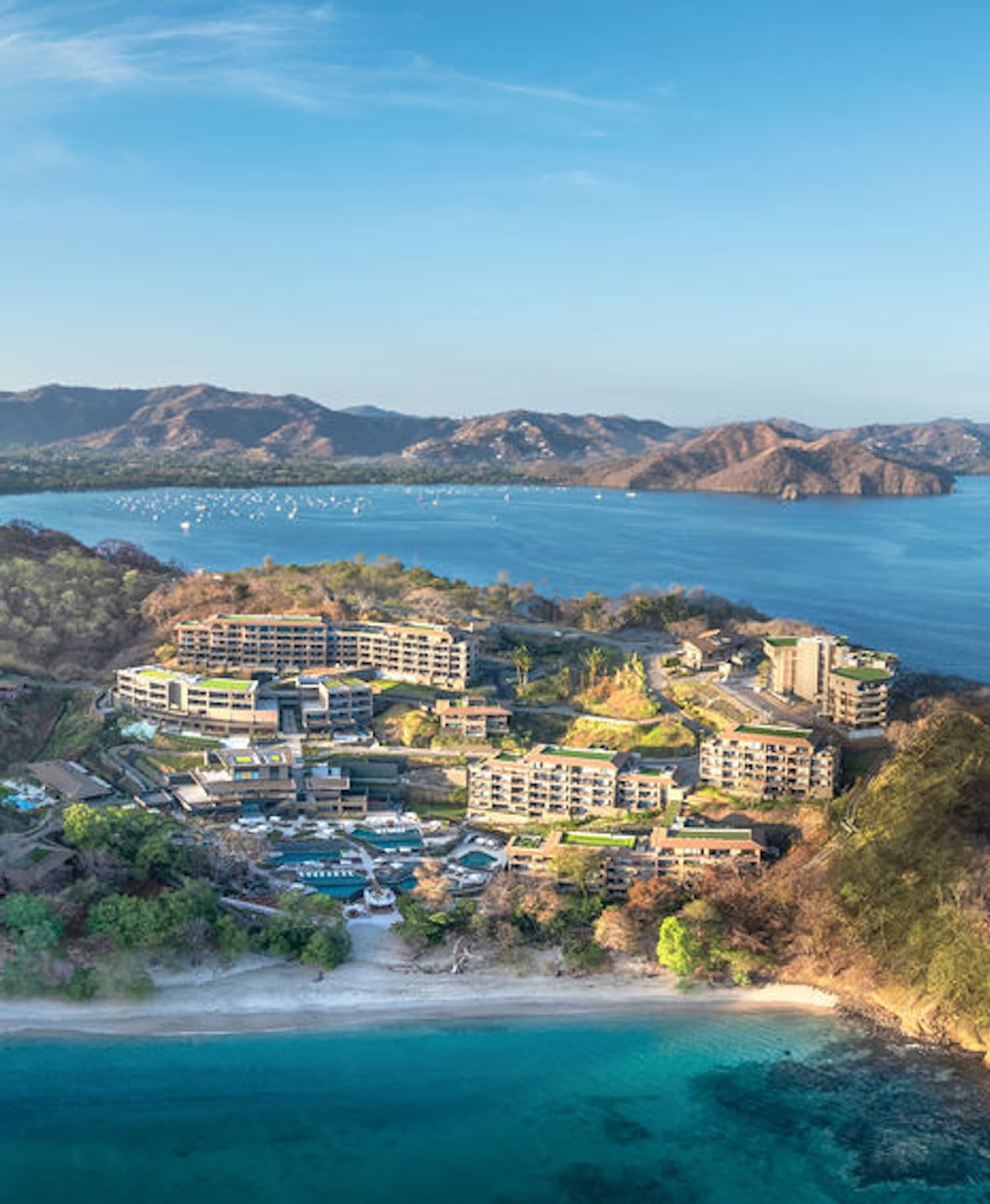 Aerial view of the Waldorf Astoria Punta Cacique hotel and residences complex built into a lush hillside, with terraced buildings, pools, and pathways overlooking the Gulf of Papagayo.