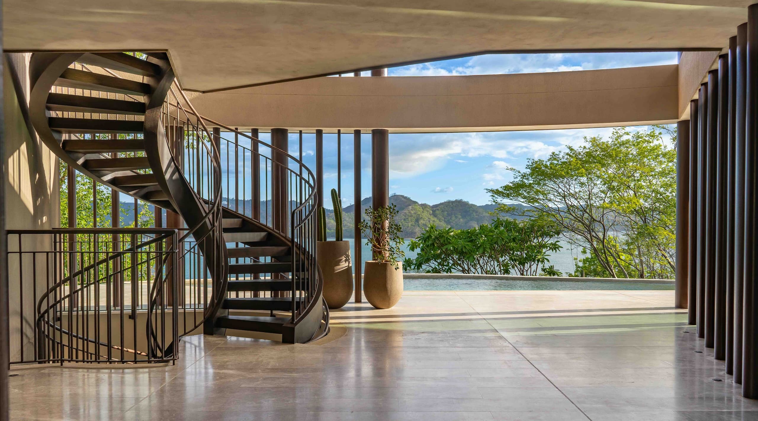 Modern hillside residence with floor-to-ceiling windows, outdoor terraces, swimming pool and warm lighting, set against tropical greenery at dusk.